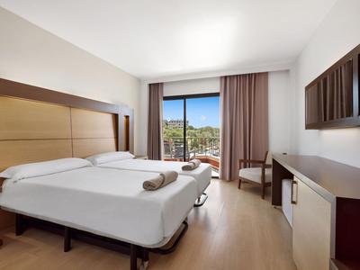 Bright hotel room with two beds, desk, and terrace overlooking greenery.