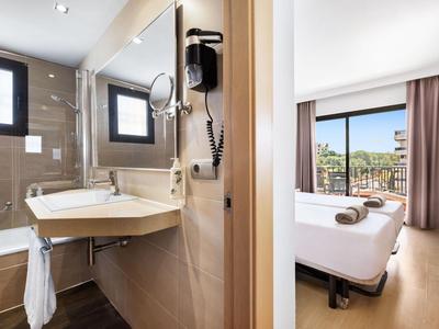 Modern hotel room with bright colors, comfortable beds, and adjacent bathroom with sink.