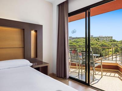 Bright hotel room with double bed and balcony overlooking green landscape.