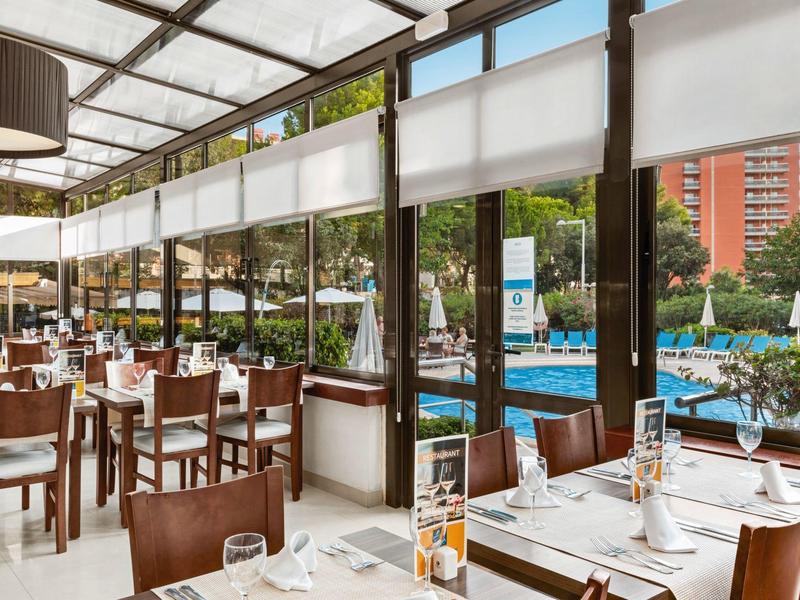 Bright restaurant with large windows overlooking a hotel pool.