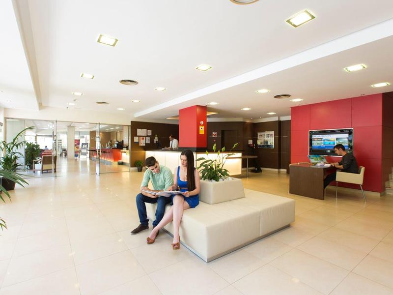 Bright hotel lobby with seating, two women relaxing, and check-in area in the background.