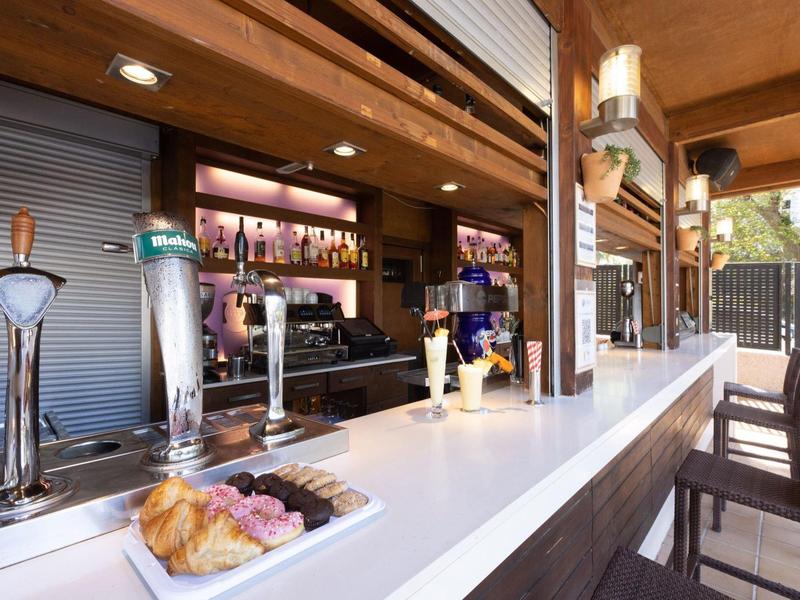 Modern outdoor bar area with wooden structure and counter featuring pastries and drinks.