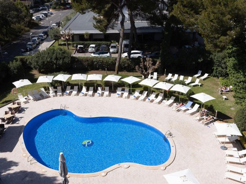 Round outdoor pool with sun loungers and umbrellas at a hotel resort.