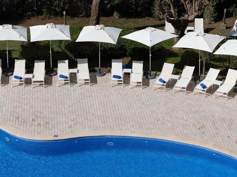Round blue pool with white lounge chairs and large umbrellas along the edge.