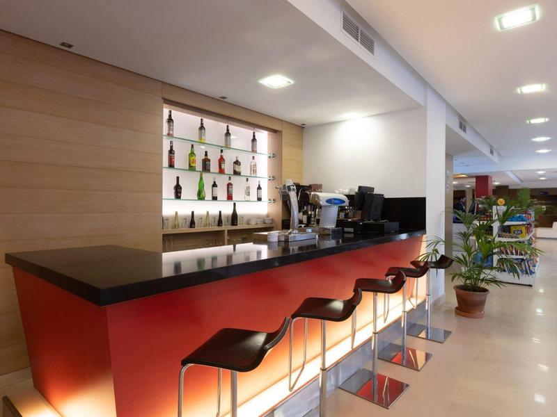 Modern hotel bar area with illuminated counter and black bar stools.