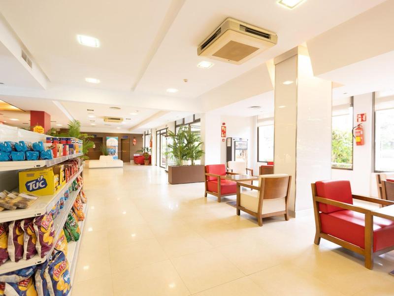 Bright hotel lobby with club chairs, snacks, and plants along the corridor.