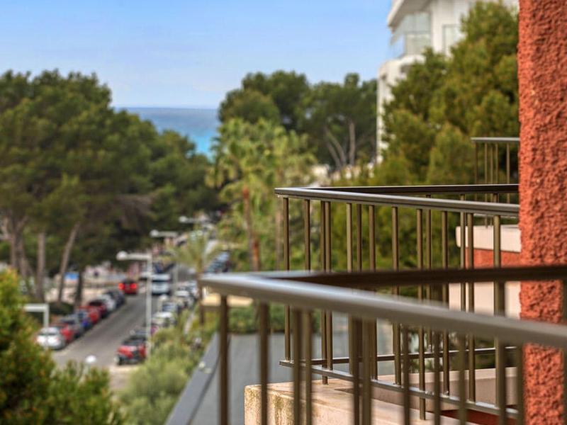 View from a balcony with metal railing onto a tree-lined street and the sea in the background.