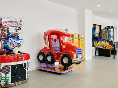 Bunte Kinderspiele in einem hellen, weißen Raum mit automatischem Fahrgeschäft und Flipperautomat.