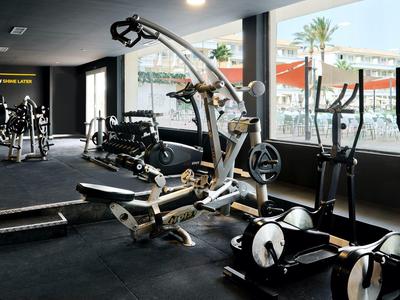 Hell erleuchteter Fitnessraum mit verschiedenem schwarzen Trainingsgerät und großen Fenstern.