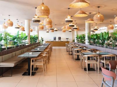 Ristorante moderno e ben illuminato con lampade sospese e piante lungo le pareti.