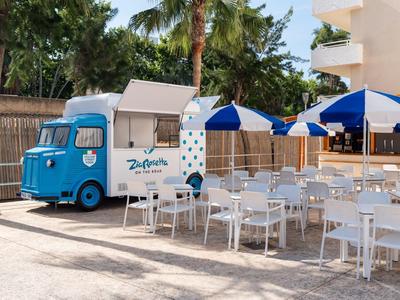 Food truck blu accanto a tavoli e sedie bianchi con ombrelloni blu all'aperto