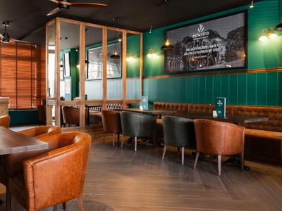 Accogliente bar dell'hotel con sedie in pelle marrone, tavoli in legno e pareti dipinte di verde.