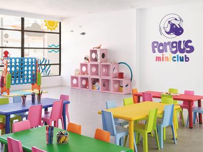 Bunter Kinderraum mit kleinen Tischen, Stühlen, Spielwand und Regal, helle freundliche Atmosphäre.