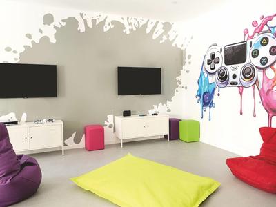 Modernes Spielzimmer mit zwei Fernsehern, bunten Sitzsäcken und heller Wanddekoration.