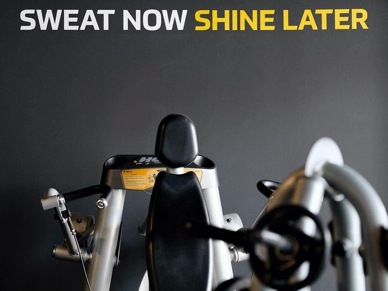 Palestra con attrezzi e muro nero con scritta "Sweat now shine later" in giallo e bianco.