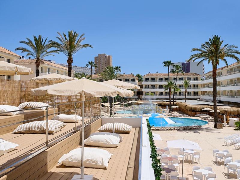 Piscina dell'hotel con palme, ombrelloni e lettini sotto un cielo azzurro.