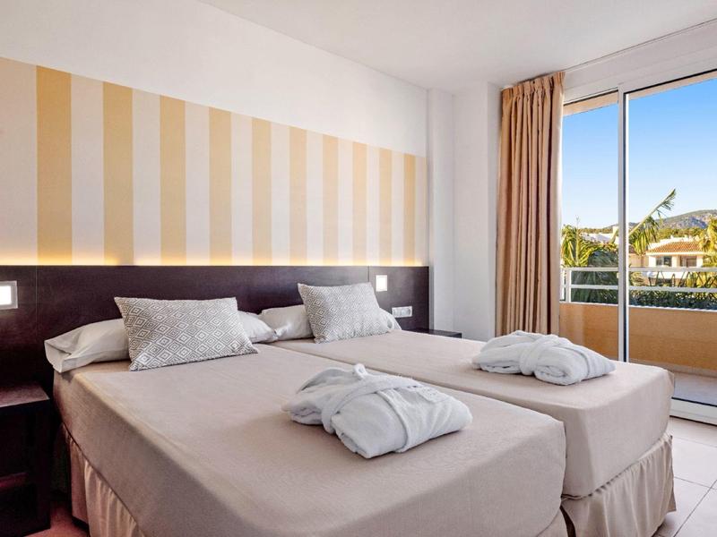 Camera d'albergo luminosa con due letti singoli e balcone con vista sulla città.