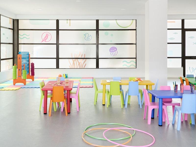 Sala giochi colorata con piccoli tavoli e sedie per bambini, luce naturale abbondante.