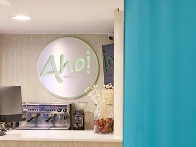 Moderner Empfang mit rundem Leuchtschild "Aho!", Computer und Dekoration auf der Theke.