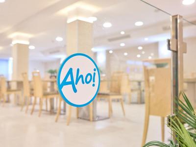 Heller, moderner Gastraum mit Holzstühlen, Tischen und grüner Pflanze im Vordergrund.