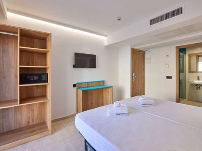 Moderner Hotelzimmer mit Doppelbett, Holzmöbeln, Wand-TV und einem Badezimmer im Hintergrund.