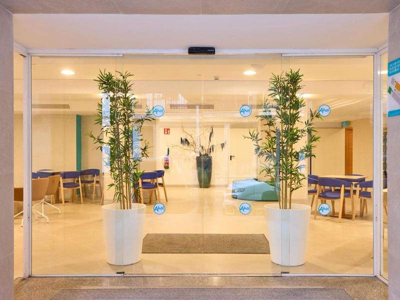 Moderner Eingangsbereich mit Glaswänden, weißen Pflanzkübeln, grünen Pflanzen und Sitzgelegenheiten.