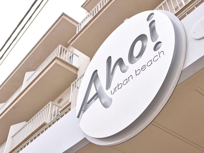 Rundes, weißes Schild mit dem Schriftzug "Ahoi urban beach" an moderner Balkonfassade.