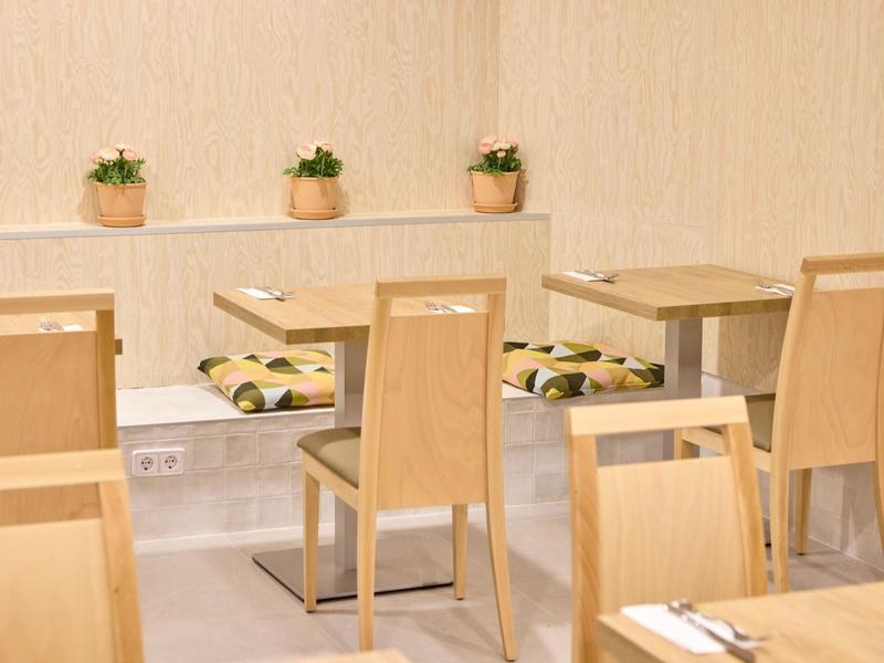 Hell eingerichteter Gastraum mit hellen Holzmöbeln und kleinen Pflanzen auf der Fensterbank.