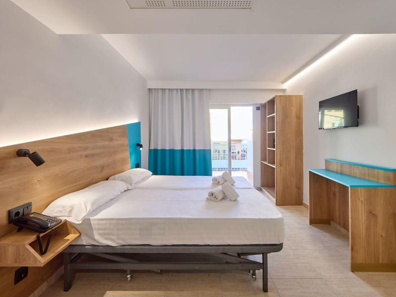 Modernes Hotelzimmer mit zwei Betten, Holzmöbeln, TV an der Wand und Balkon mit Meerblick.