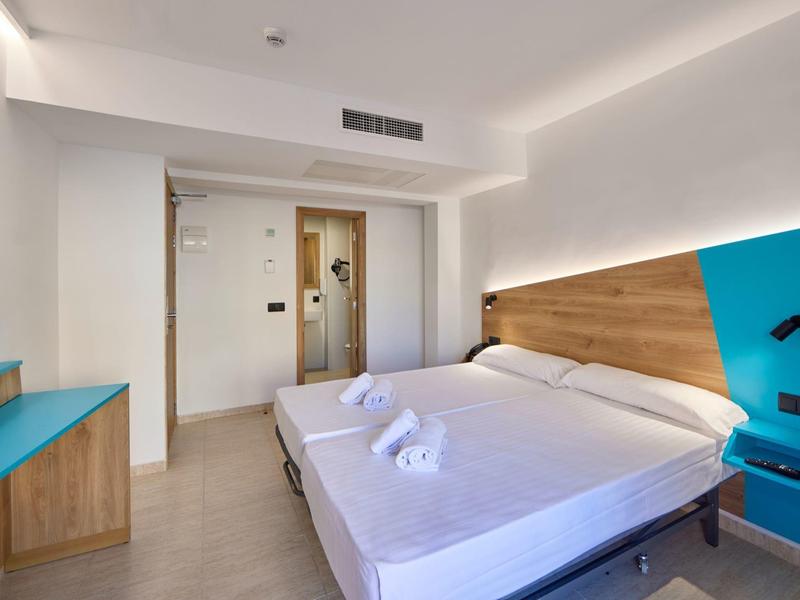 Modernes Hotelzimmer mit Doppelbett, Holzdetails, blauen Akzenten und einfachem Design.