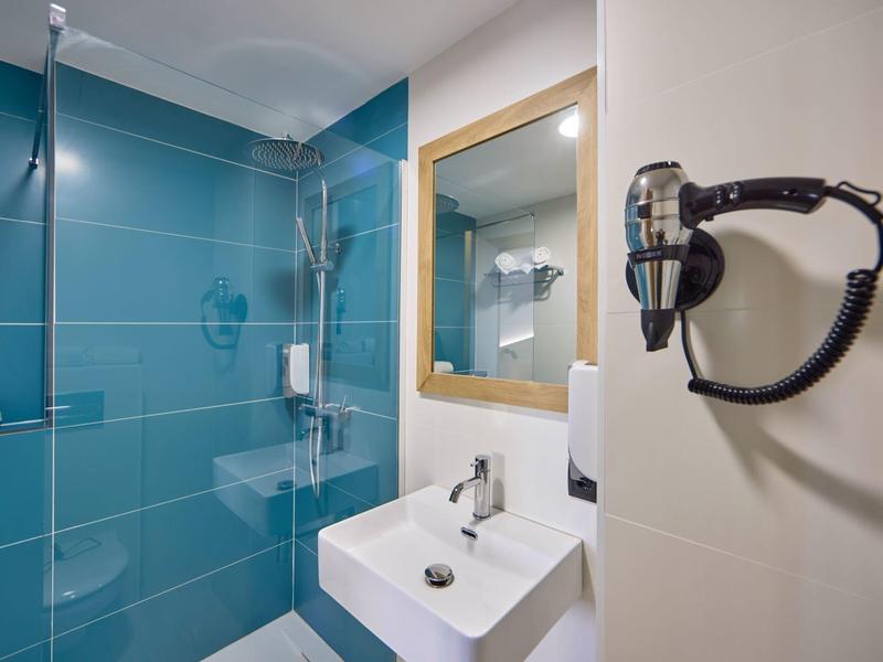 Modernes Badezimmer mit blau gekachelter Dusche, weißem Waschbecken, Spiegel und Wand-Föhnhalter.