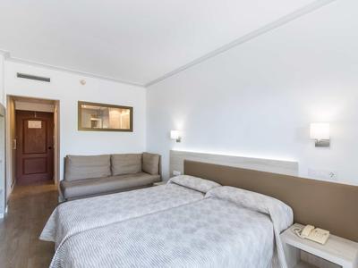 Modern hotel room with double bed, sofa, wooden floor, and simple decor.