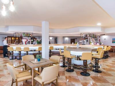 Bright hotel bar area with counter, bar stools, and seating groups on patterned floor.