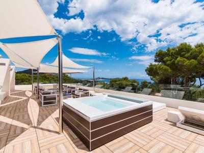 Terrasse mit Holzdeck, Whirlpool, weißen Sonnenschirmen und Meerblick unter blauem Himmel.