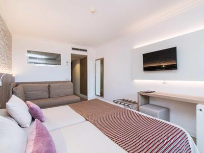 Modern hotel room with double bed, sofa, wall-mounted TV, and desk.