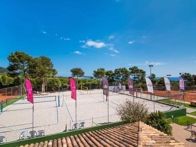 Several sand volleyball courts with colorful flags under a clear blue sky next to a building.