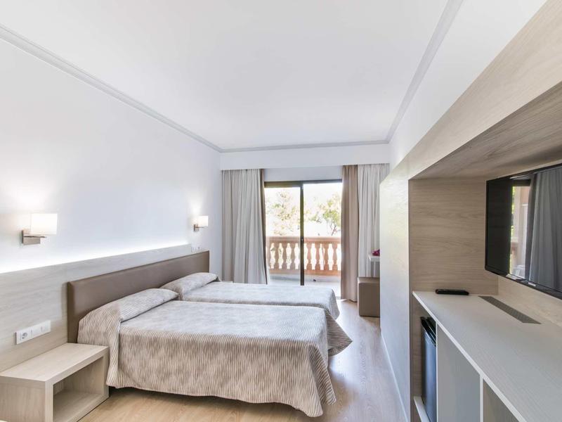 Bright hotel room with double bed, balcony, and wall-mounted flat-screen TV.