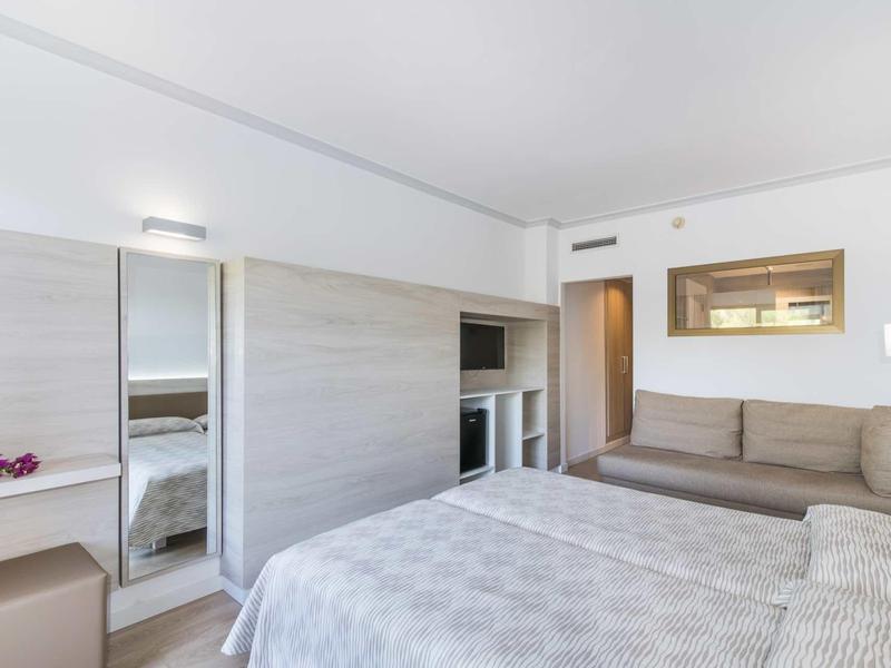 Modern hotel room with double bed, sofa, and closet with mirror and TV.