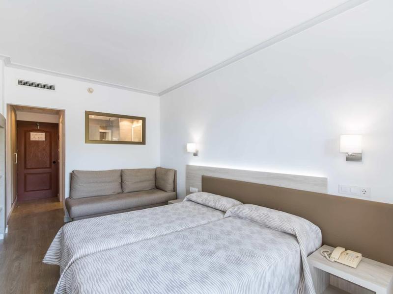 Modern hotel room with double bed, sofa, wooden floor, and simple decor.