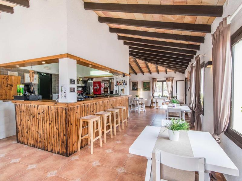 Bright guest area with wooden bar, stools, and tables with white chairs by windows.