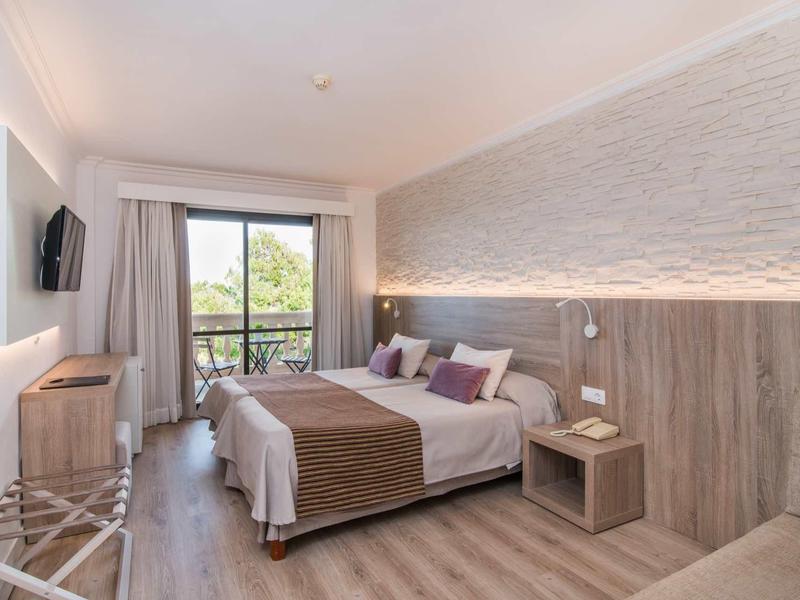 Modern hotel room with double bed, wood flooring, balcony, and wall-mounted TV.