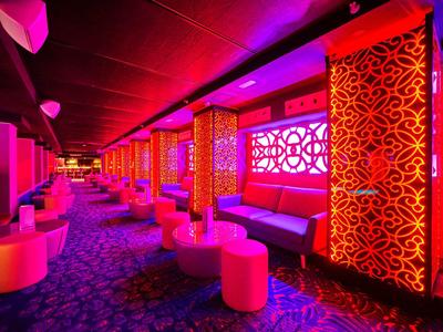 Kleurrijke lounge met ingewikkelde rode patronen en zachte zitplaatsen onder paarse verlichting.