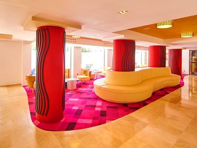 Moderne hotel lobby met rode pilaren, een lange gele gebogen bank en een rood patroon tapijt.