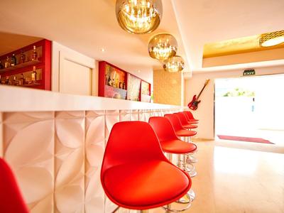 Moderne hotelbar met opvallende rode stoelen, witte getextureerde bar en warm licht.