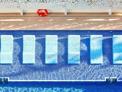 Zes witte ligstoelen op een rij in een blauw zwembad met een reddingsboei op het terras.