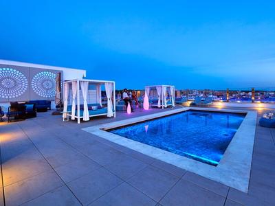 Dakterras met zwembad, loungebedden en stadszicht onder een heldere avondlucht.