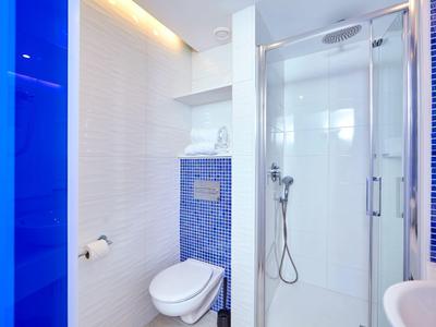 Moderne hotelbadkamer met witte en blauwe tegels, douchecabine, toilet en wandgemonteerde toiletrolhouder.