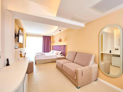 Lichte hotelkamer met bed, bank, wandspiegel en een lang wit bureau bij het raam.