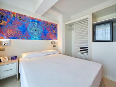 Moderne hotelkamer met wit bed, kleurrijke wanddecoratie en ingebouwde kast.