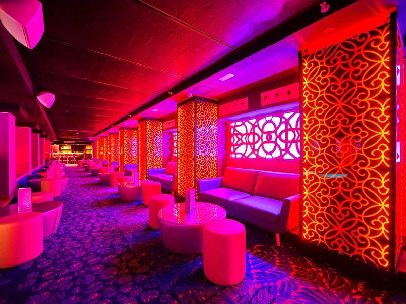 Kleurrijke lounge met ingewikkelde rode patronen en zachte zitplaatsen onder paarse verlichting.